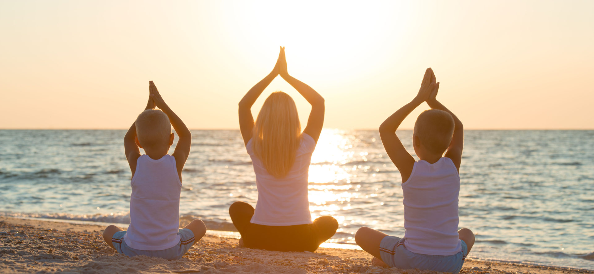Two kids and a woman doing a yoga pose on the beach