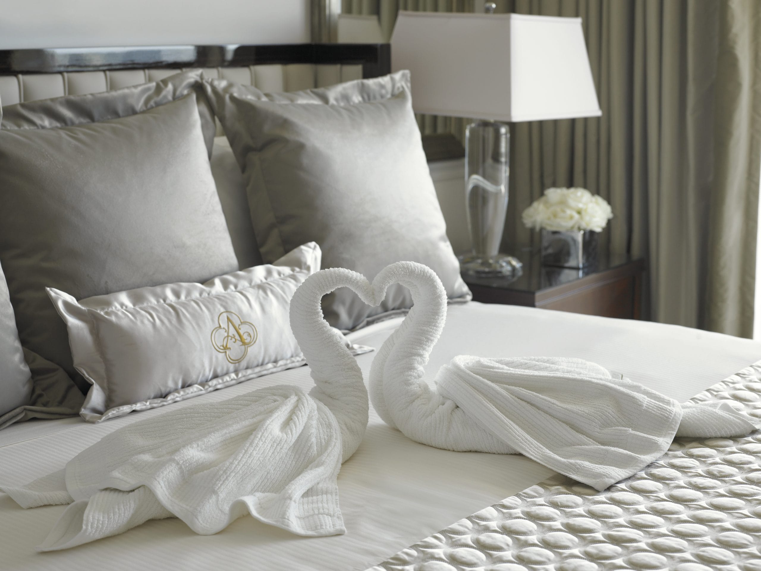 Luxury hotel bed featuring elegant linens, decorative swan-shaped towel art, plush pillows, and refined furnishings at Acqualina Resort Miami Beach.