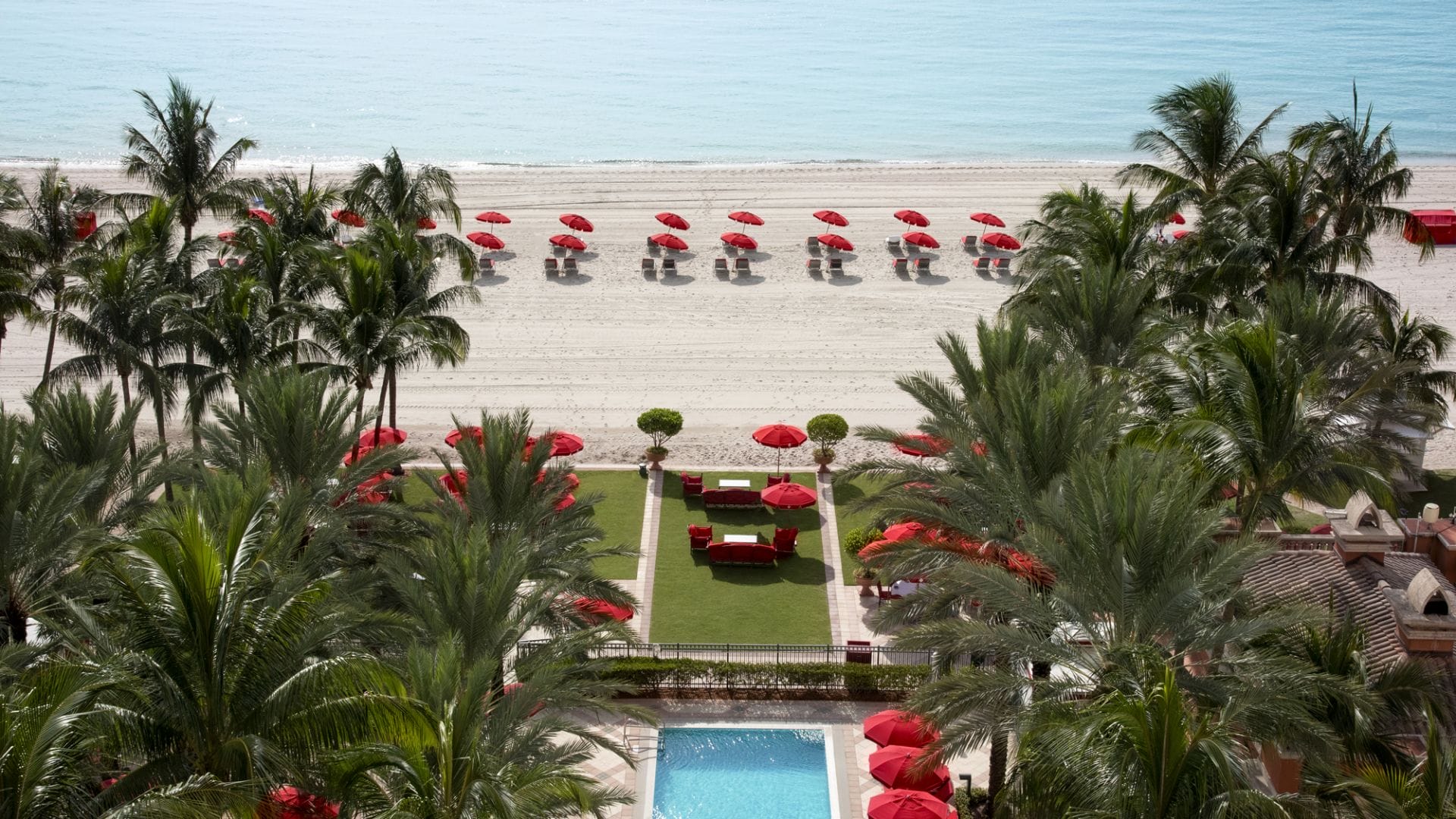 aerial view of luxury beachfront resort with palm trees and red umbrellas