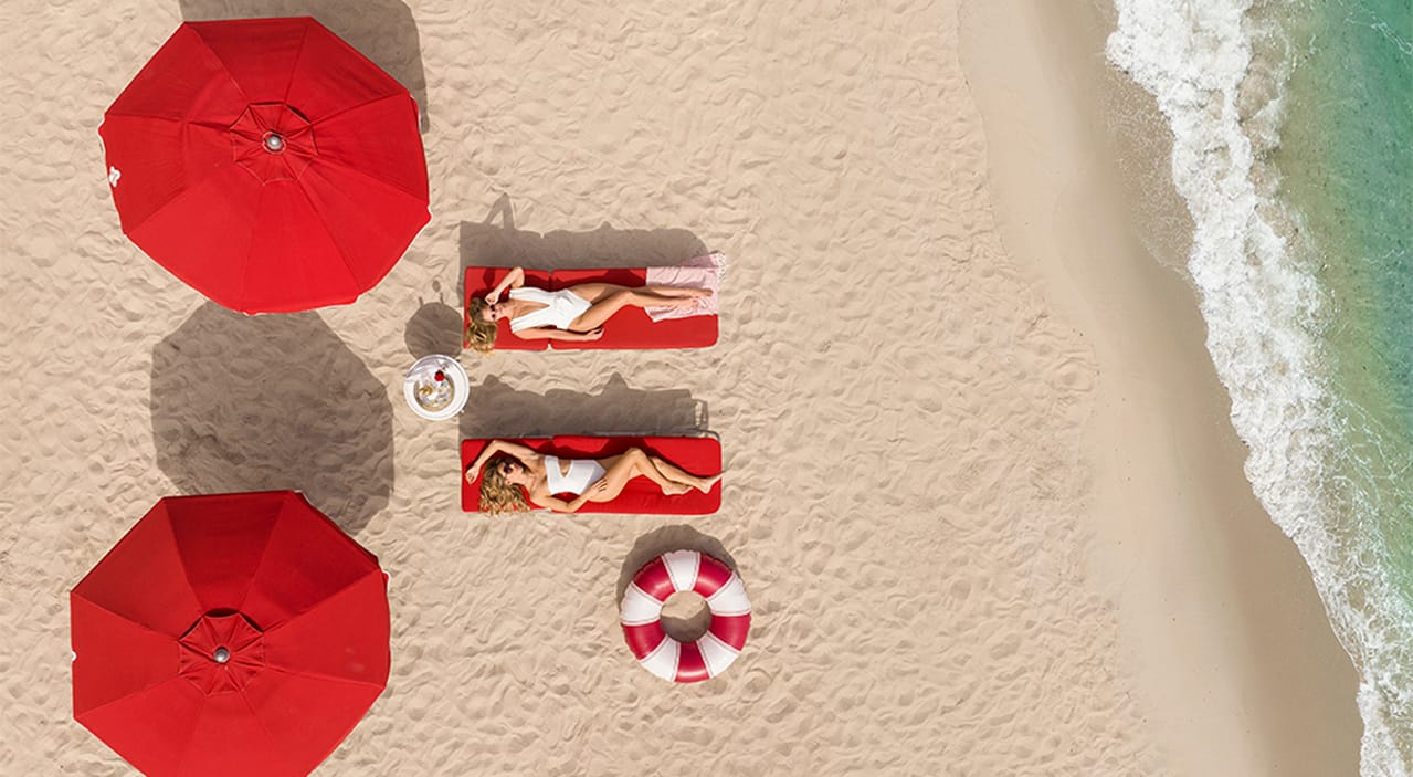 Two women lying on red loungers on the beach.